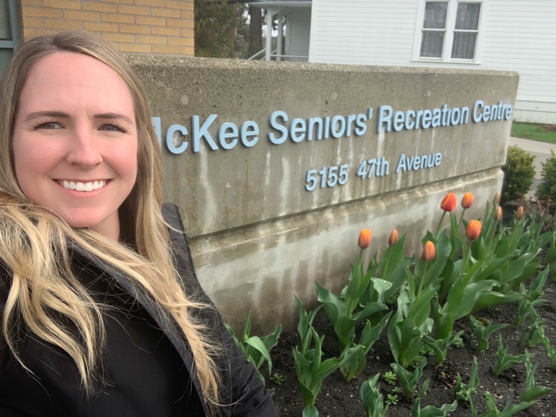 Woman smiling in front of sign that reads: McKee Seniors Recreation Centre